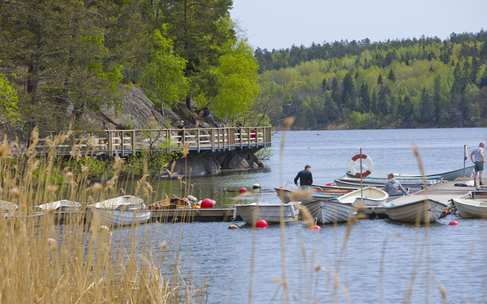 En brygga med flera småbåtar och en gångbro längs berget vid vattnet.