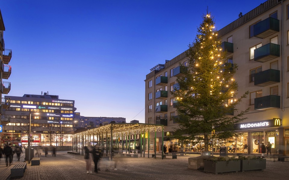 Liljeholmstorget med julbelysning och en stor julgran, fotat i skymning.