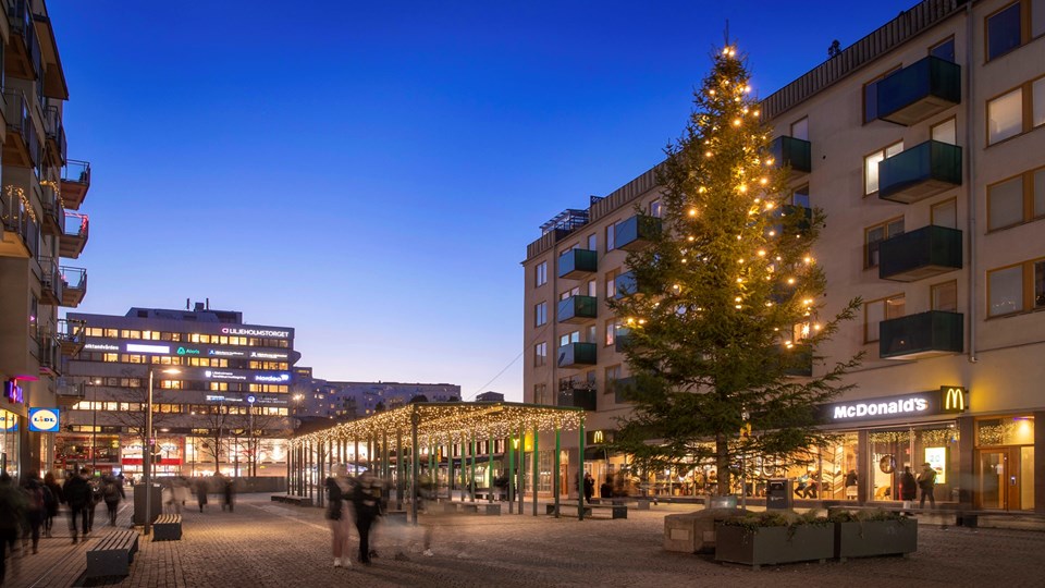 Liljeholmstorget med julbelysning och en stor julgran, fotat i skymning.
