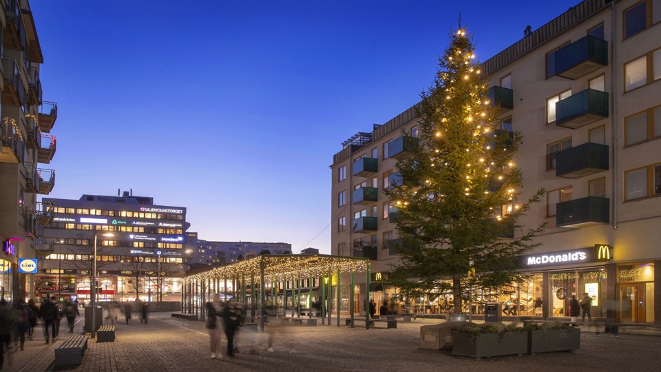 Liljeholmstorget med julbelysning och en stor julgran, fotat i skymning.