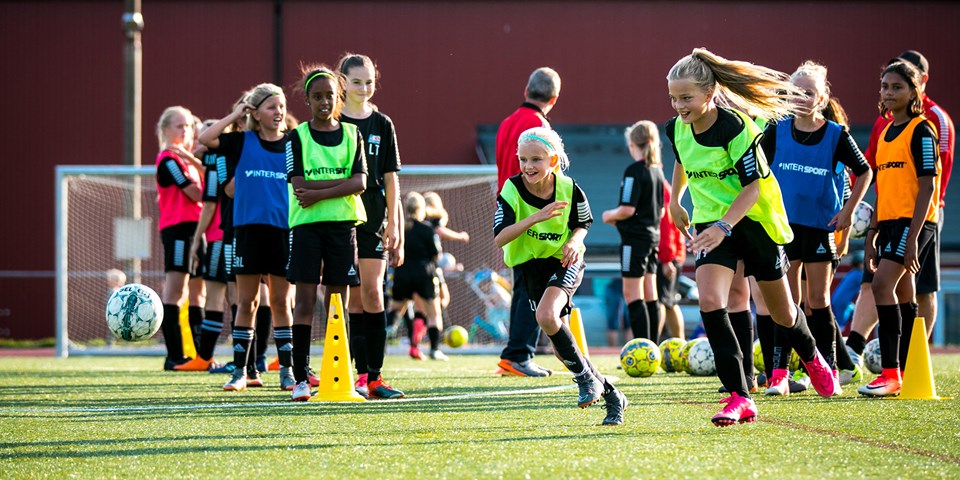 Flickor tränar fotboll på en konstgräsplan.