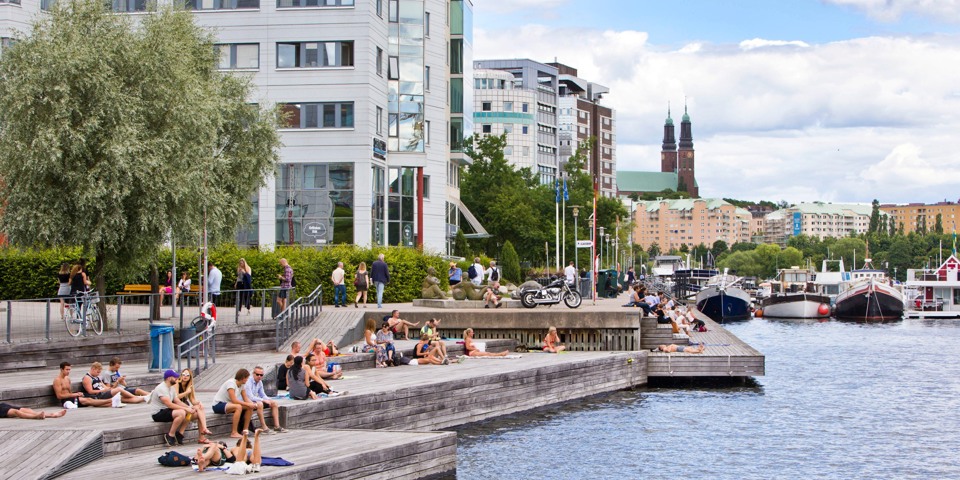 Människor som solar vid stora soldäck längs vattnet vid Liljeholmskajen.