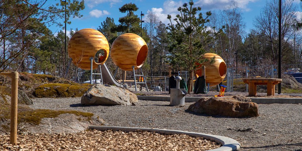 Park med modern lekplats i närhet till skog.