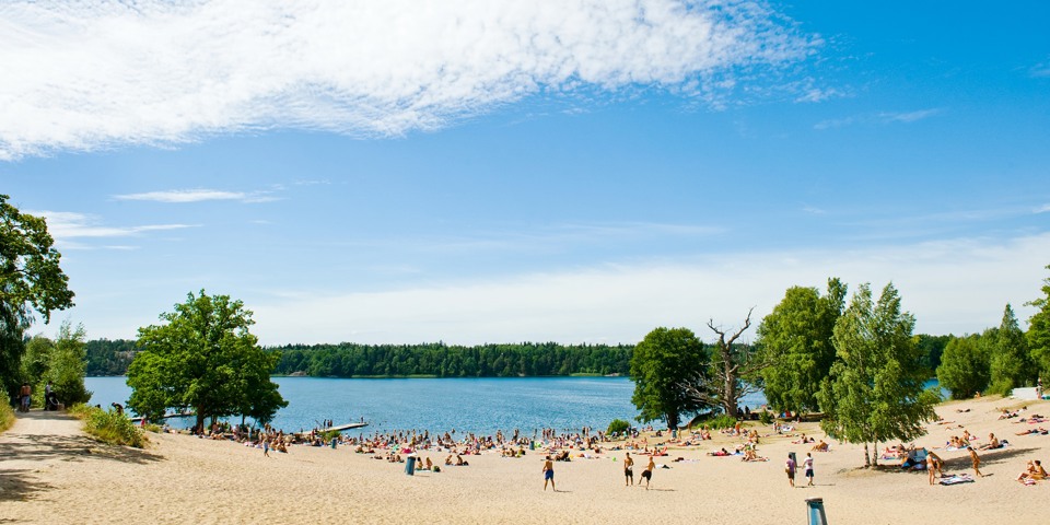 En stor sandstrand med många besökare som leker i sanden eller ligger och solar.