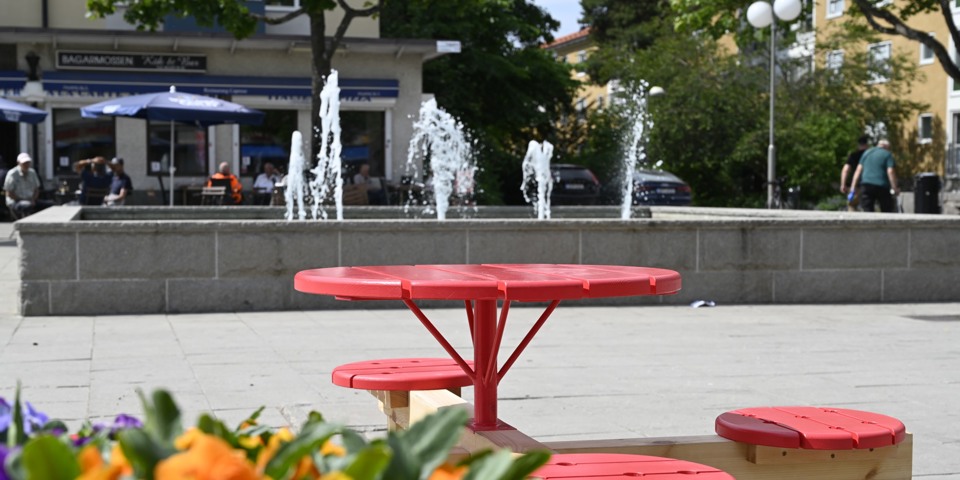 Ett torg med blommor, sittplatser och en stor fontän.