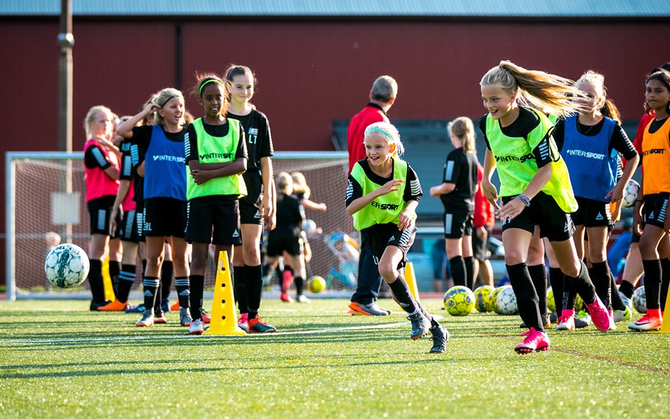 Flickor tränar fotboll på en konstgräsplan.