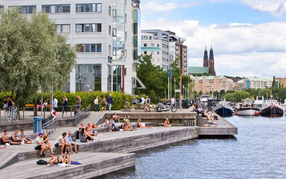 Människor som solar vid stora soldäck längs vattnet vid Liljeholmskajen.