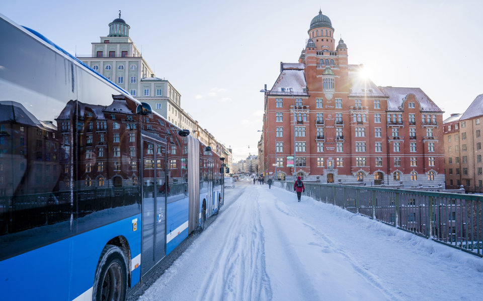 Buss som kör över en bro en vinterdag. Människor som promerar längs bron. Foto.