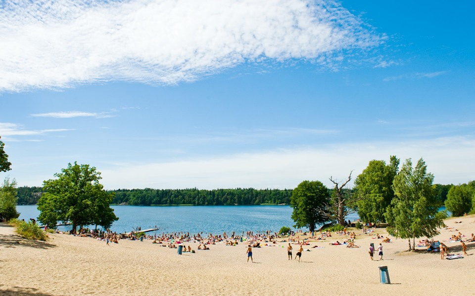En stor sandstrand med många besökare som leker i sanden eller ligger och solar.