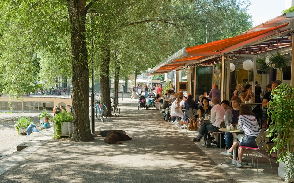 Björns trädgård, Södermalm. En sommardag med grönskande träd. Människor sitter i parken och äter på restaurangerna intill.