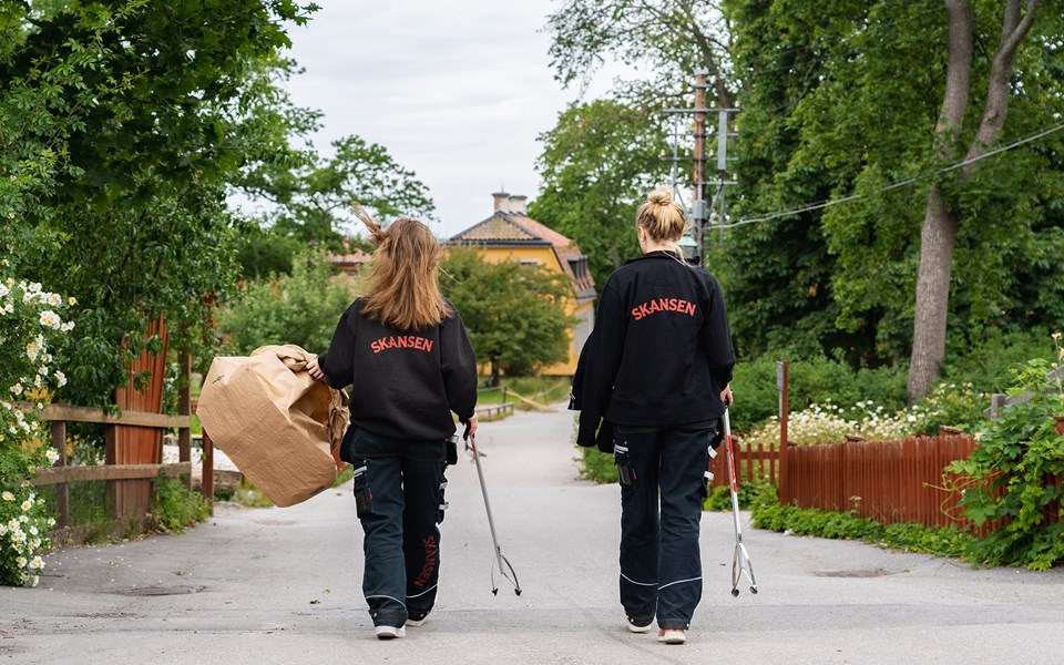 Två arbetande personer som går och plockar skräp inne på Skansen.